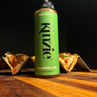 Kinzie Jalapeño Lime BBQ Sauce bottle with food items on a wooden surface