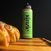 Kinzie Jalapeño Lime BBQ Sauce bottle on a wooden surface with tacos in the background