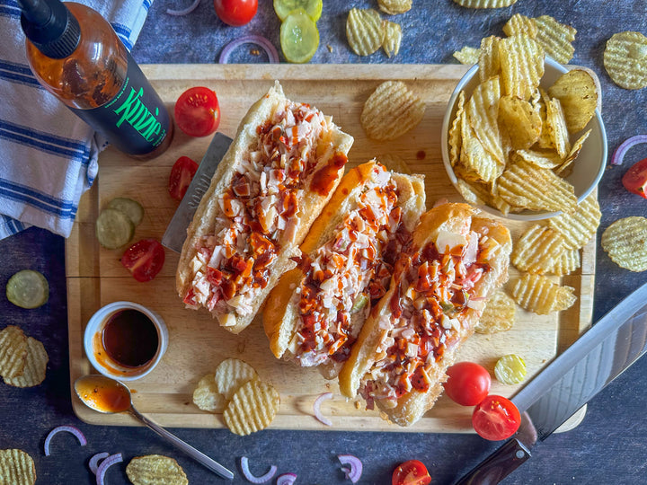 Wooden cutting board with sandwiches and chips on a dark surface