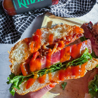 Sandwich with bacon and lettuce on a wooden board, with a bottle of ketchup in the background.