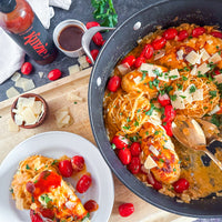 Spaghetti dish with cherry tomatoes and cheese in a pan, with a bottle of sauce on the side.