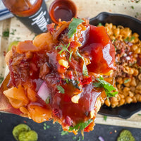 Close-up of a dish with meat and vegetables on a wooden spoon, with pasta in the background.