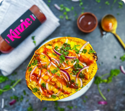 Spaghetti squash boat with toppings on a dark surface with Kinnie branding.