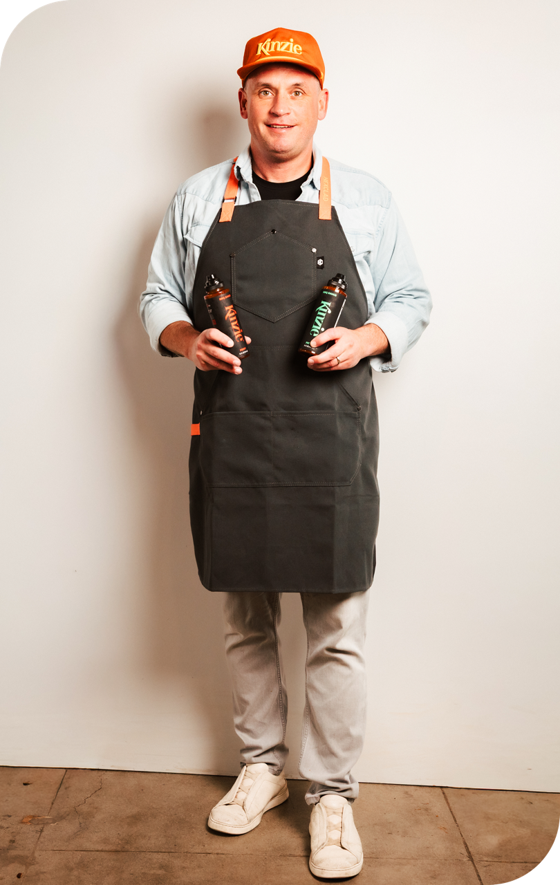Man wearing an apron and holding bottles against a plain background